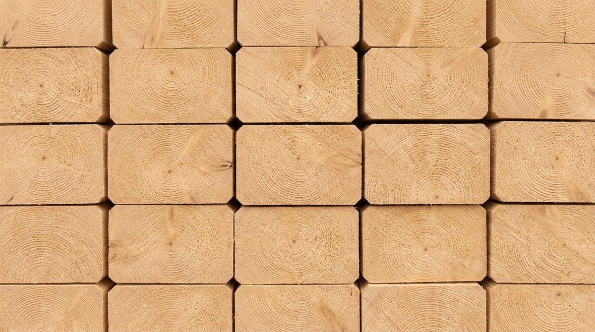 A stack of sawn softwood framing pieces seen end on, every piece the same rectangular cross section, growth rings showing in the end grain